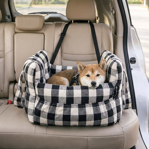 Small dog resting in a black check pet car bed on a rear car seat, straps looped around the headrest